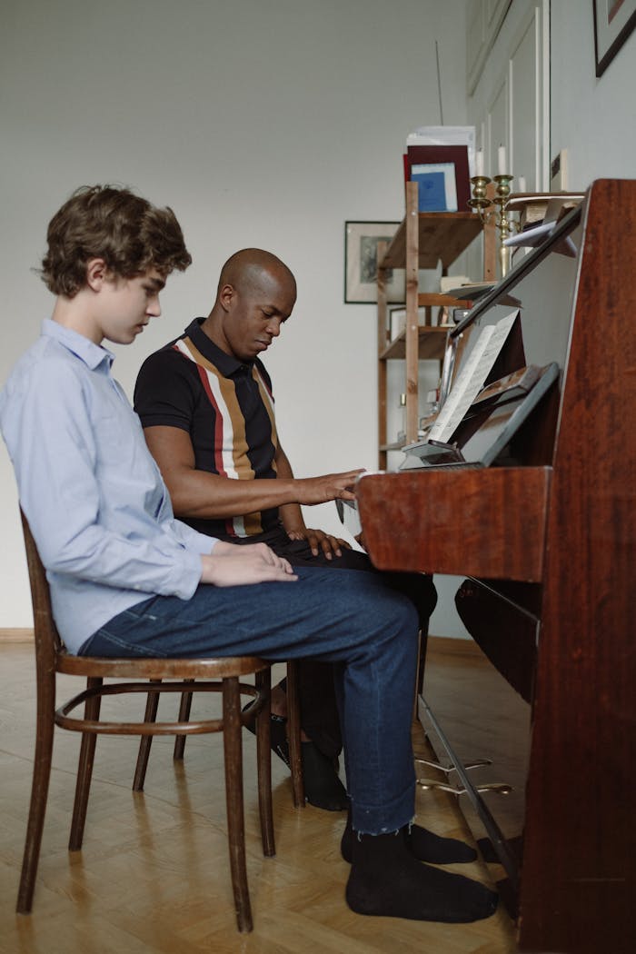 gallery-2 A teacher instructs a student during a piano lesson indoors, both focused on playing.