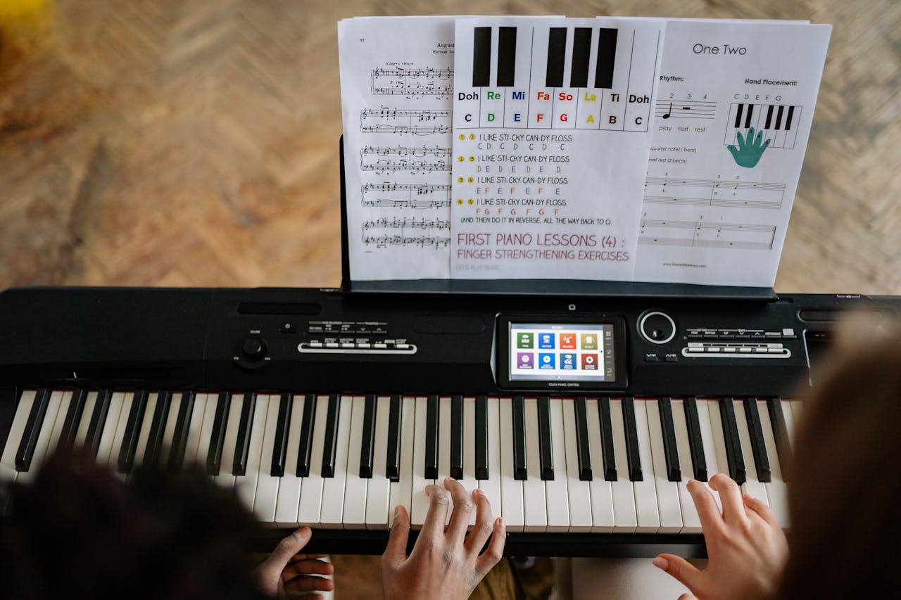 our-services-1 Adults learning piano with music sheets, viewed from above.